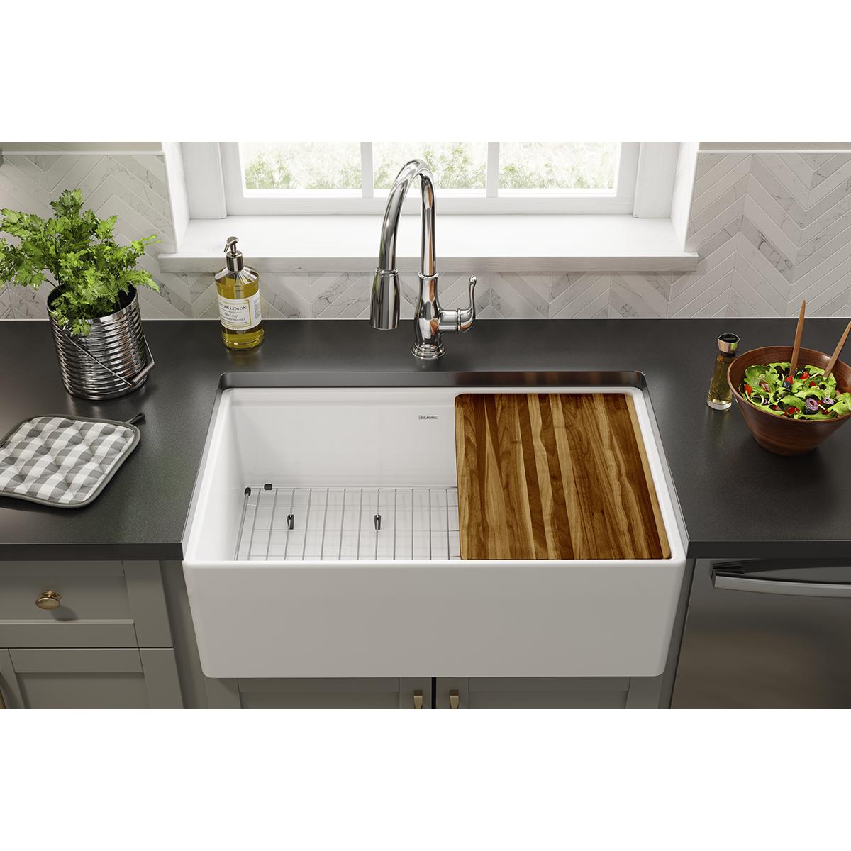 Stainless steel sink grid with slotted left section and solid wood cutting board right section installed in white farm sink.