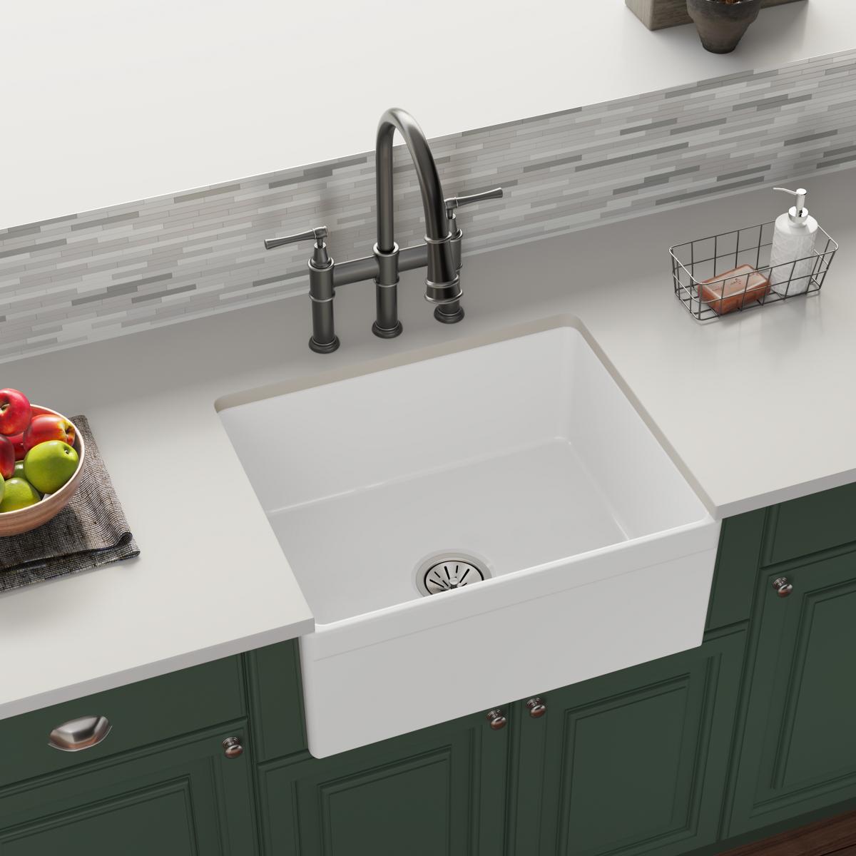 White fireclay farmhouse sink with single bowl and apron front installed in green cabinetry.