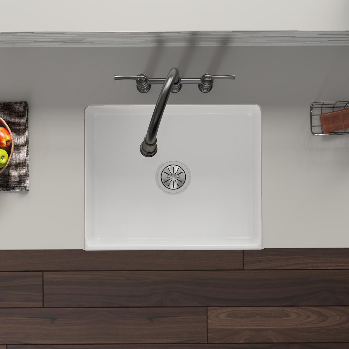 Stainless steel drain assembly with strainer basket installed in white fireclay sink, shown from above.