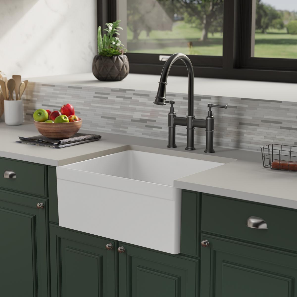 White fireclay farmhouse sink with single deep bowl installed in green cabinetry with black faucet.