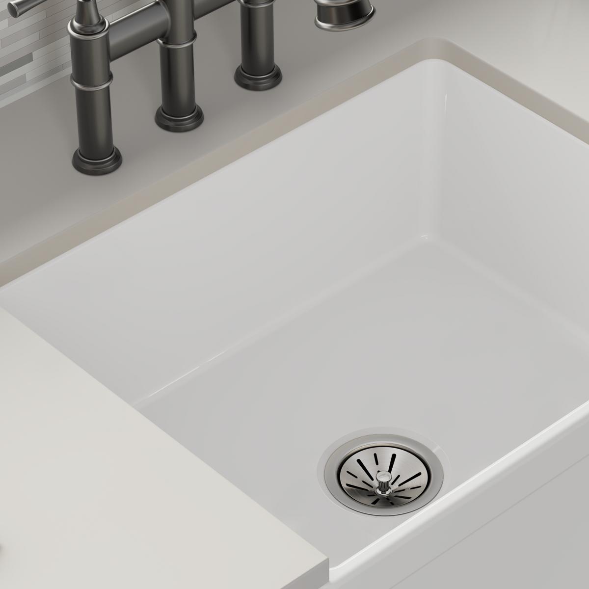 White fireclay single bowl farmhouse sink with drain strainer and stainless steel faucet mounted on countertop.