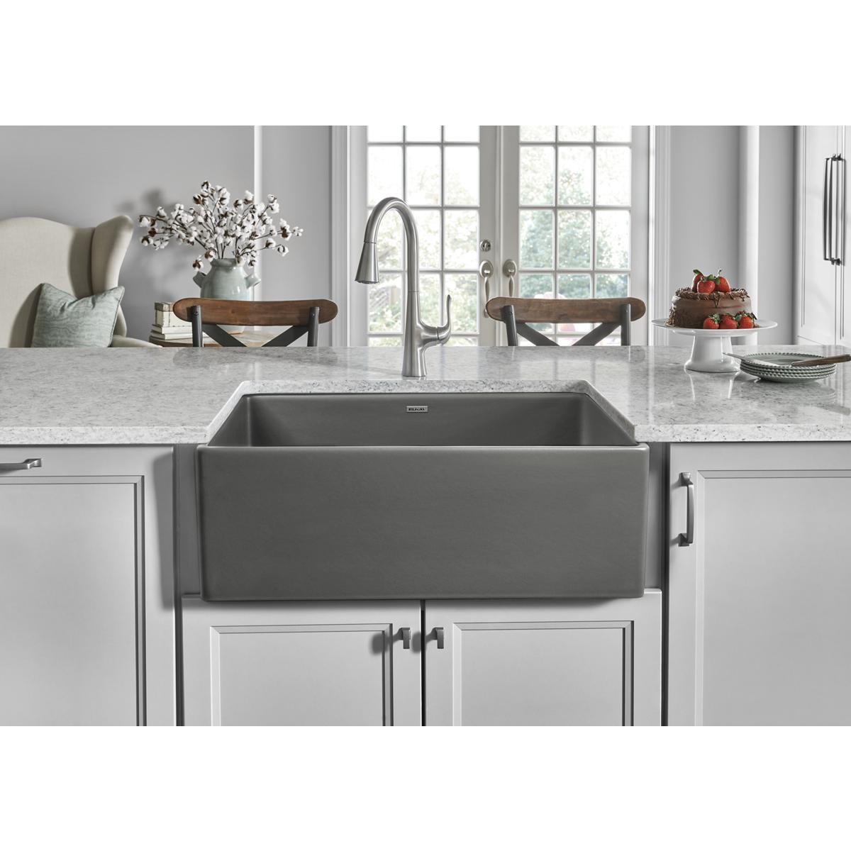 Gray fireclay single-bowl farmhouse sink with curved front apron installed in white cabinet below marble countertop.