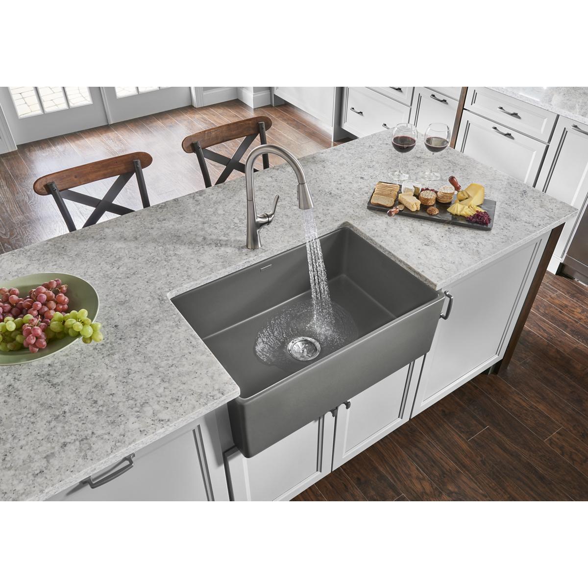 Gray fireclay farmhouse sink with single bowl installed in white kitchen countertop with faucet.
