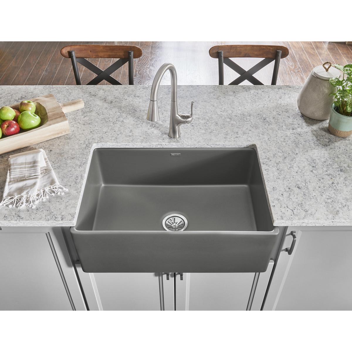 Gray fireclay single bowl farmhouse sink with apron front mounted in countertop with faucet.