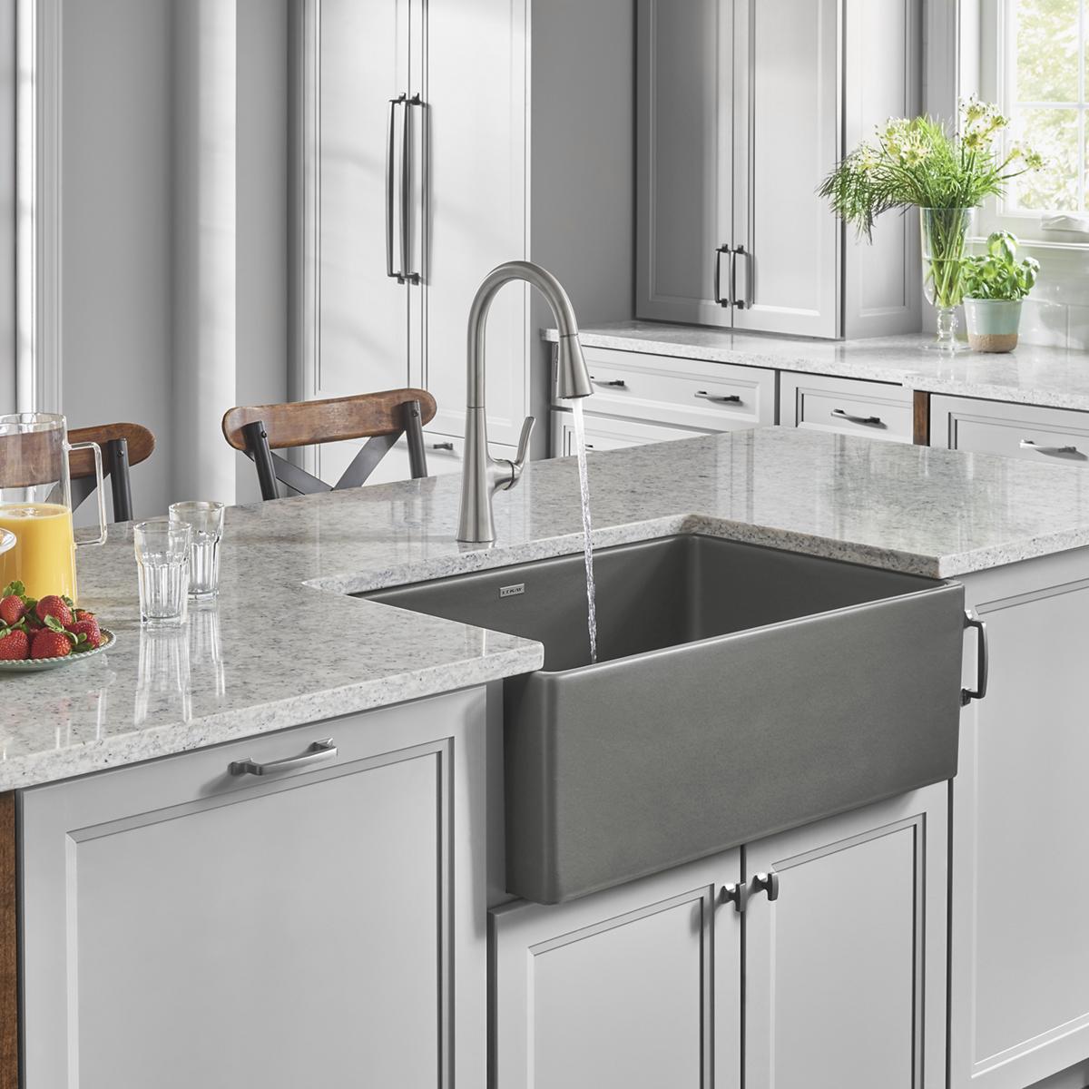 Gray fireclay farmhouse sink with single bowl and apron front installed in white kitchen countertop.