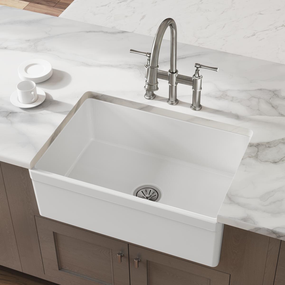 White fireclay farmhouse sink with single bowl and stainless steel faucet installed in marble countertop.