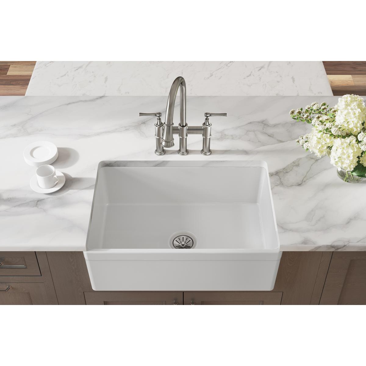 White fireclay farmhouse sink with single bowl and chrome faucet installed in marble countertop.