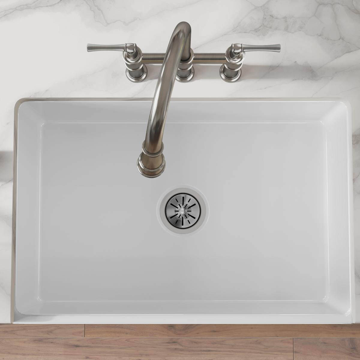 White fireclay farmhouse sink with single bowl, rounded corners, and stainless steel faucet with handles.
