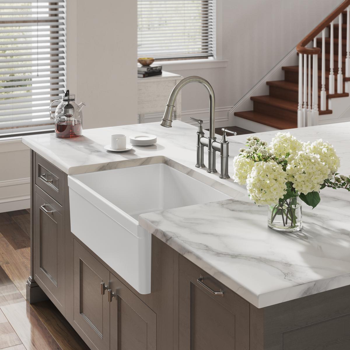 White fireclay single-bowl farmhouse sink with apron front installed in marble countertop with faucet.