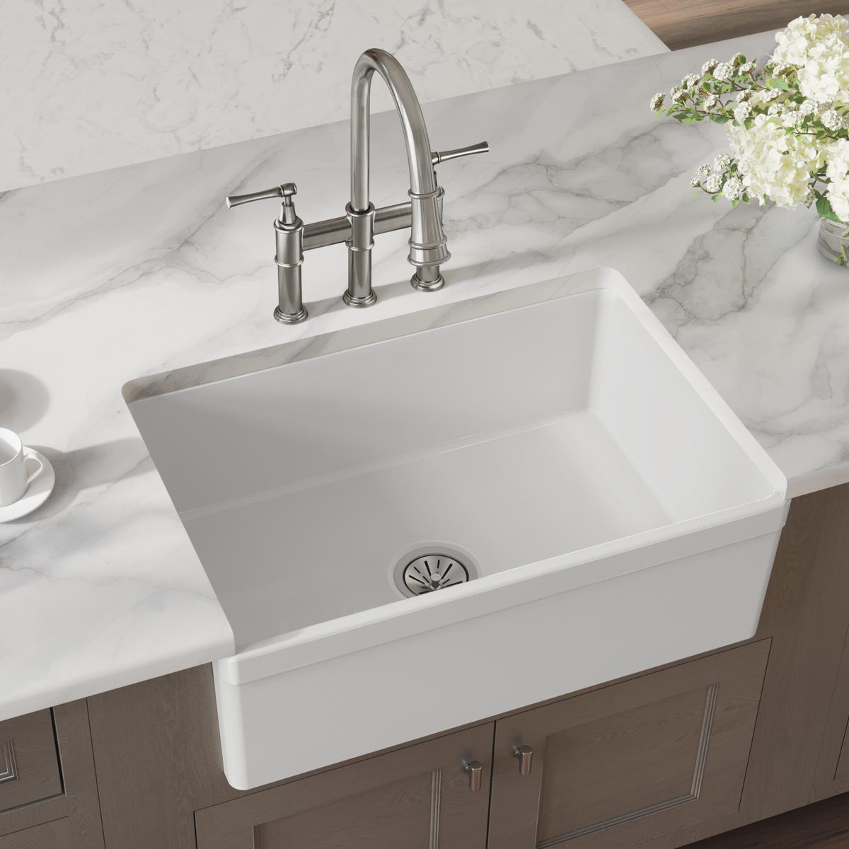 White fireclay farmhouse sink with single bowl and stainless steel faucet installed on marble countertop.