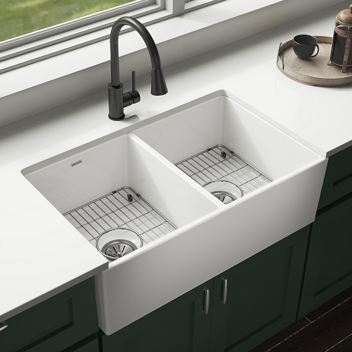 White fireclay farmhouse sink with two equal bowls, black faucet, and stainless steel grids installed in countertop.