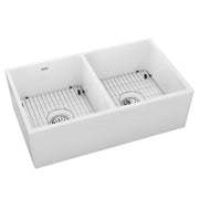 White fireclay farmhouse sink with two equal bowls, drain strainers, and metal basin grids.