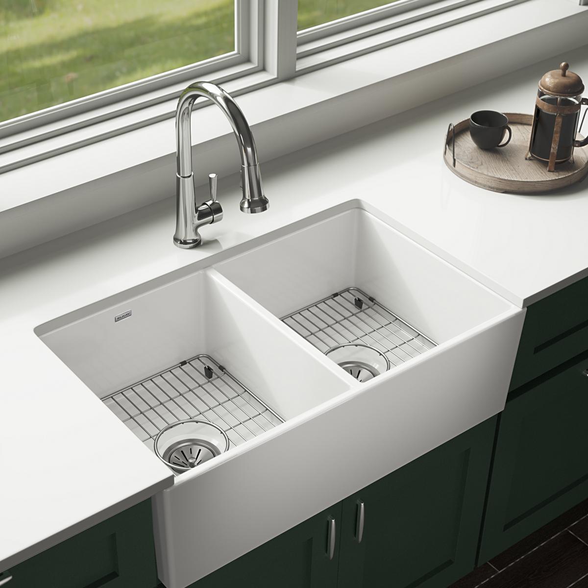 Stainless steel grid insert fitted in right basin of white farmhouse sink with drain.
