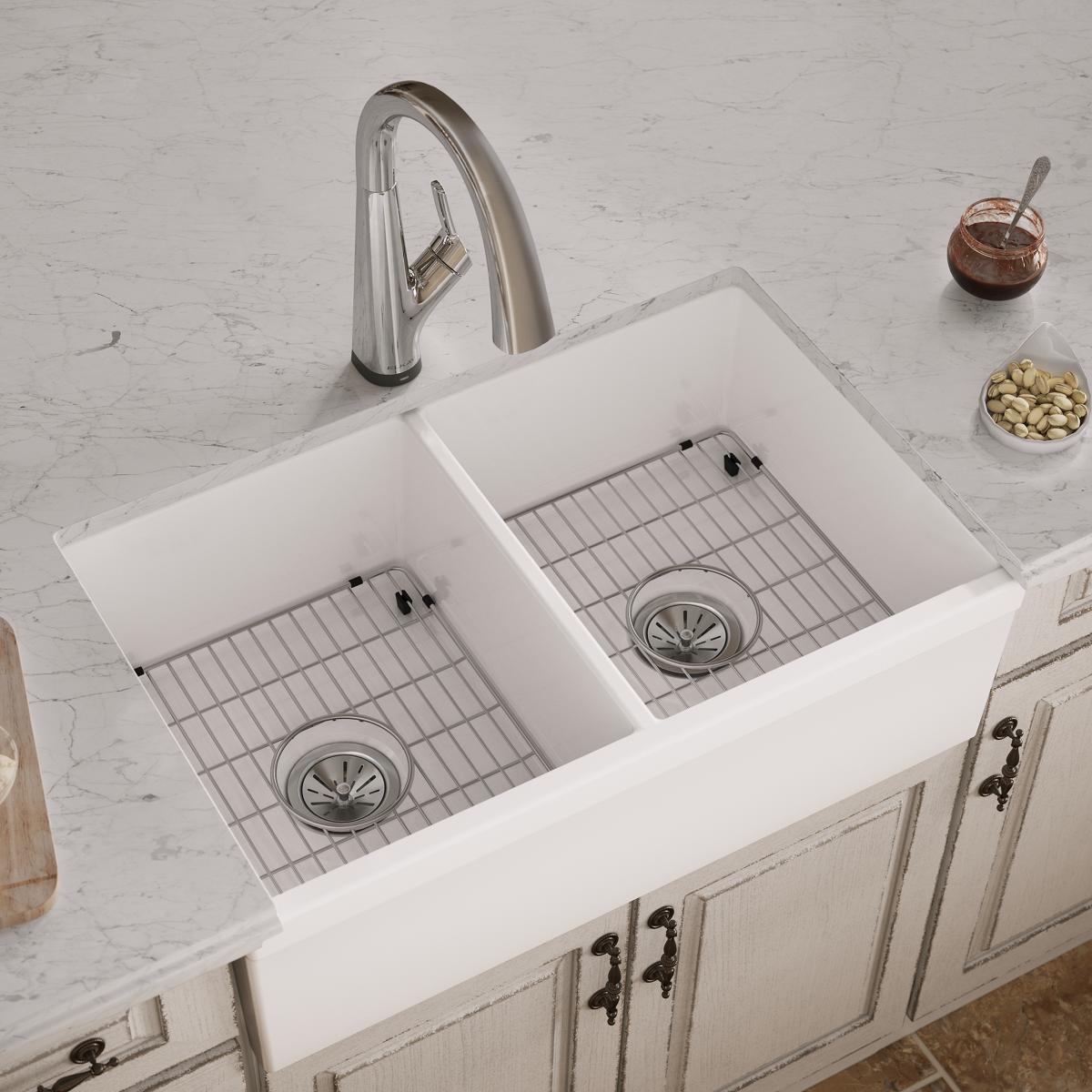 White fireclay farmhouse sink with two equal bowls, metal grid inserts, and chrome arched faucet on marble countertop.