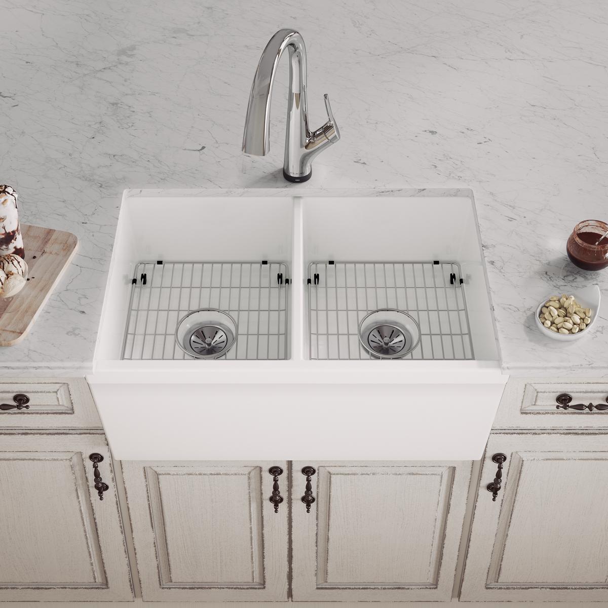 White fireclay farmhouse sink with two equal bowls, stainless steel faucet, and grid strainers installed in marble countertop