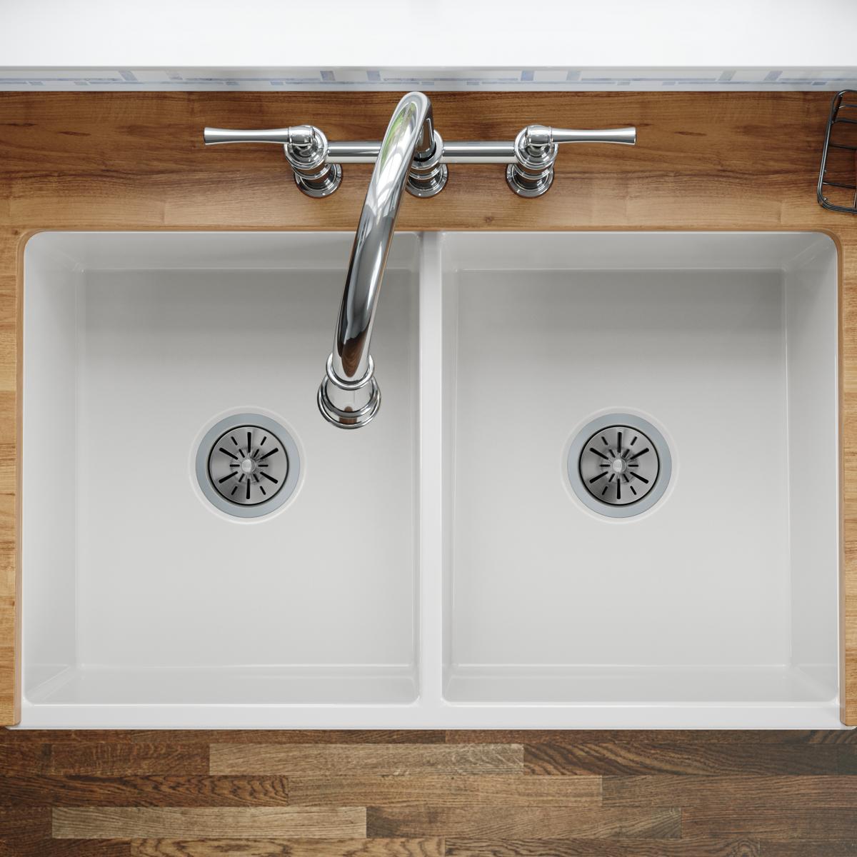 White fireclay farmhouse sink with two equal bowls, chrome faucet, and drain strainers installed in wood countertop.