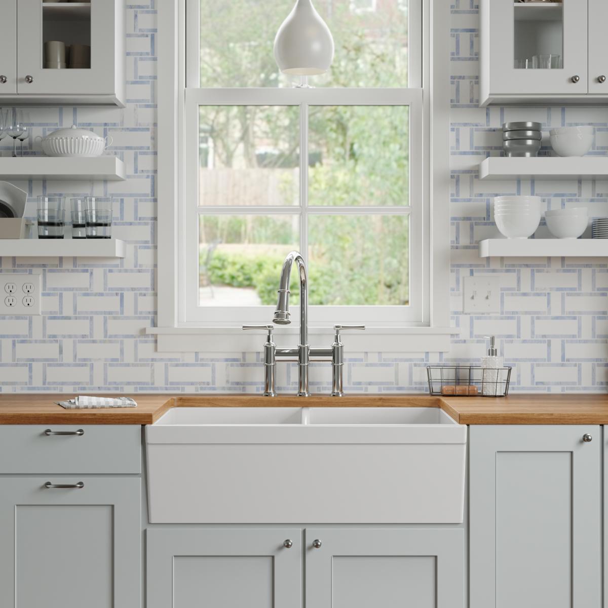 White fireclay farmhouse sink with two equal bowls installed in kitchen cabinetry with chrome faucet.
