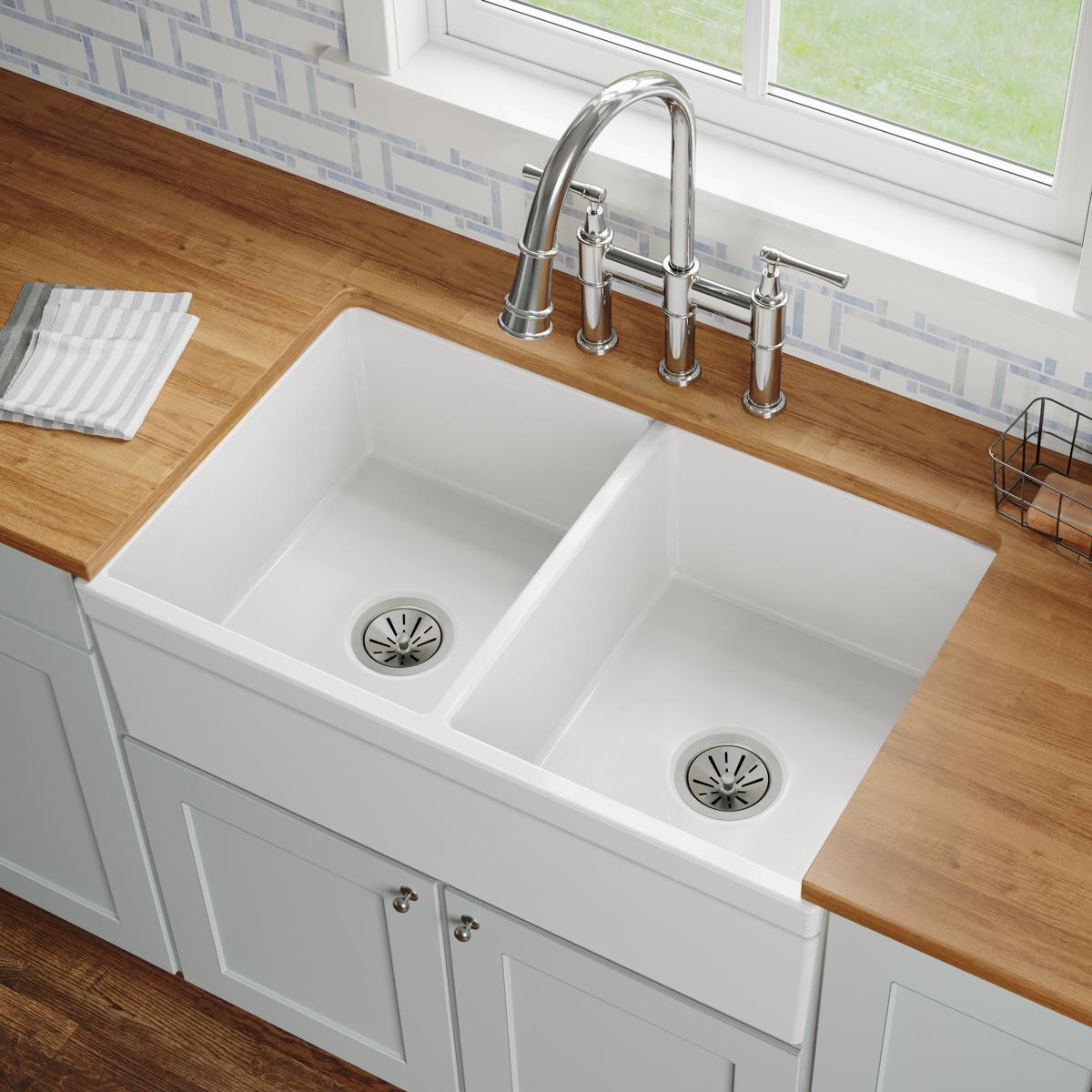 White fireclay farmhouse sink with two equal bowls, drain strainers, and chrome faucet installed in wood countertop.