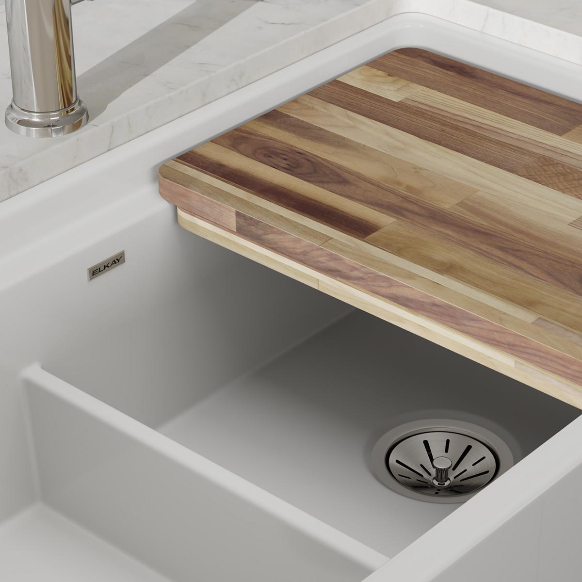White fireclay farmhouse sink with two unequal bowls, wooden cutting board divider, and metal drain strainer.