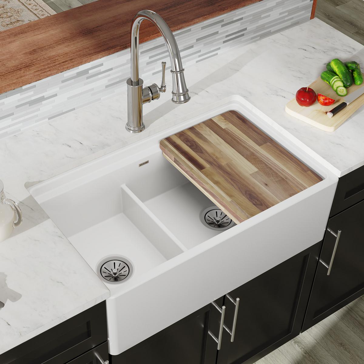 White fireclay farmhouse sink with two unequal bowls, wooden cutting board divider, and chrome faucet installed in marble cou