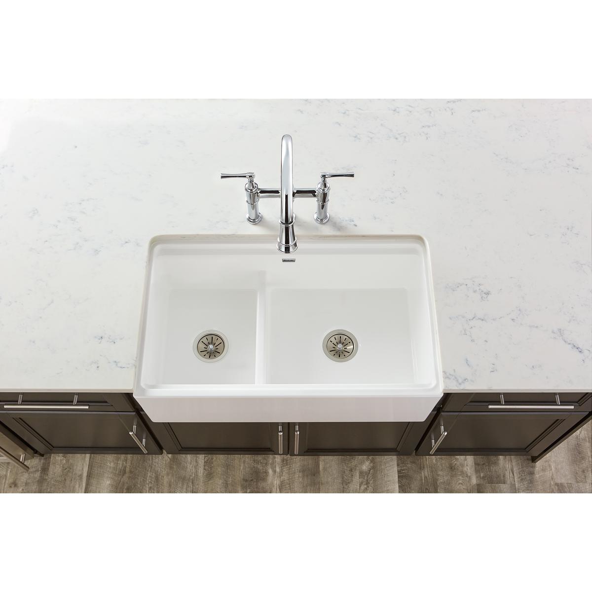 Satin finish stainless steel drain assembly with strainer basket installed in white fireclay double-basin sink.