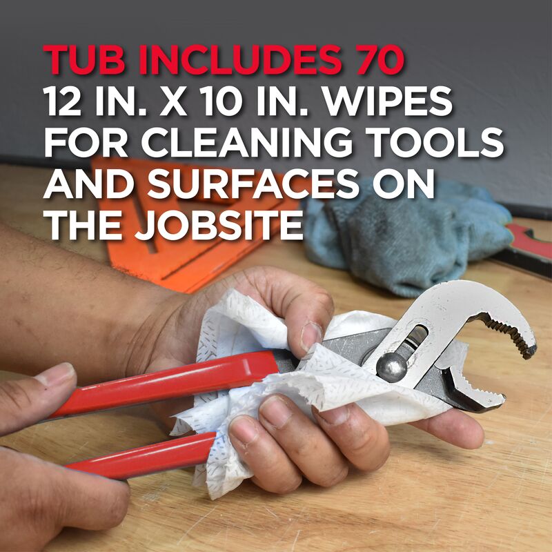 Hand holding red wrench wrapped in white pre-moistened towel on wooden surface with tools nearby.
