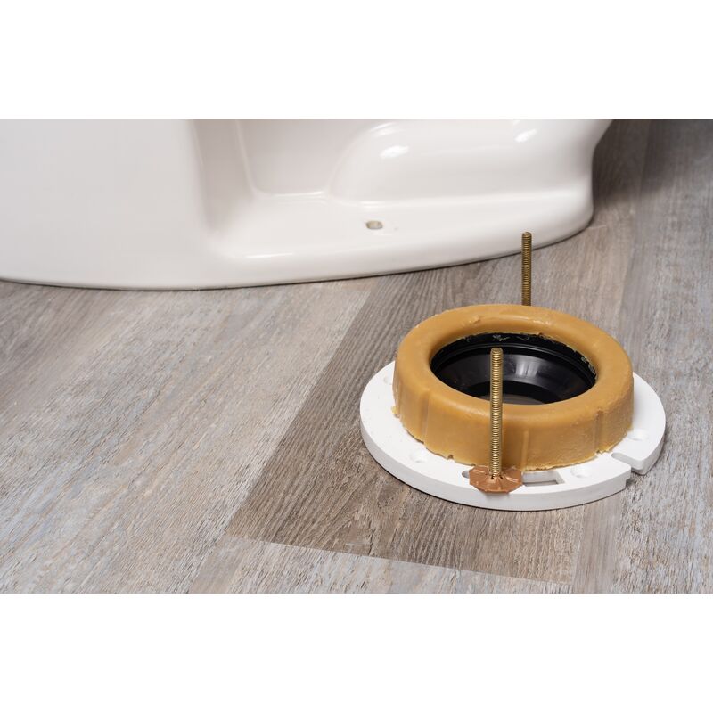 Yellow wax ring with white plastic base and brass horn bolt positioned next to toilet base on wood-grain floor.