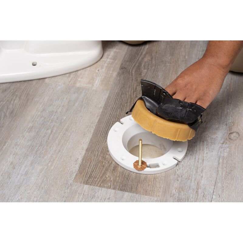 Yellow wax ring with plastic horn being installed around toilet flange opening on wooden floor.