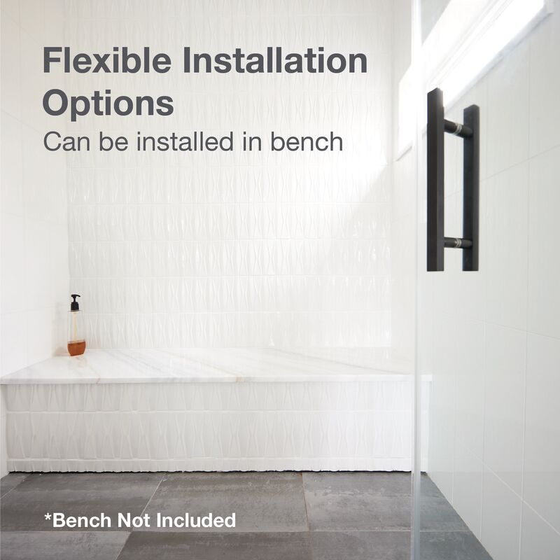 Stainless steel wall drain with vertical outlet mounted on bathroom wall above bench.