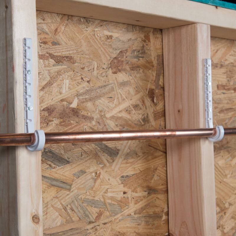 Gray plastic J-hooks securing a copper pipe to wooden framing and OSB sheeting.