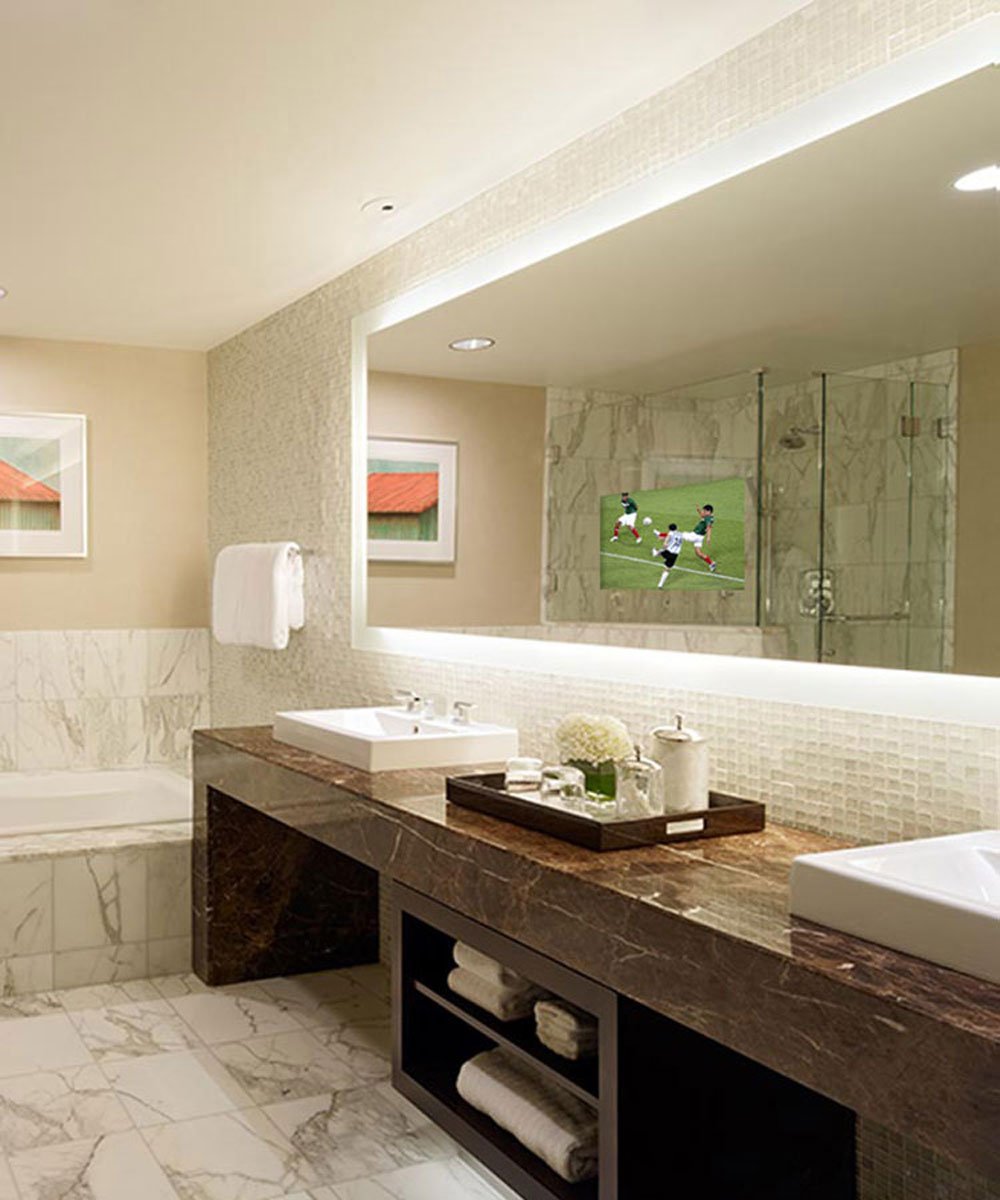 Illuminated bathroom mirror with integrated 15-inch display showing soccer match, LED edge lighting, and marble vanity instal