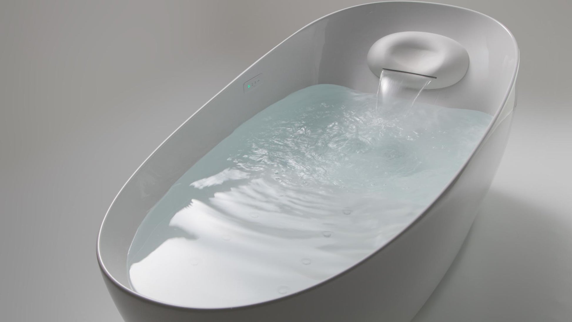 Gloss white oval bathtub with integrated faucet and water flowing into basin.