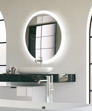 Oval lighted mirror with white LED border mounted above black vanity sink in bathroom.