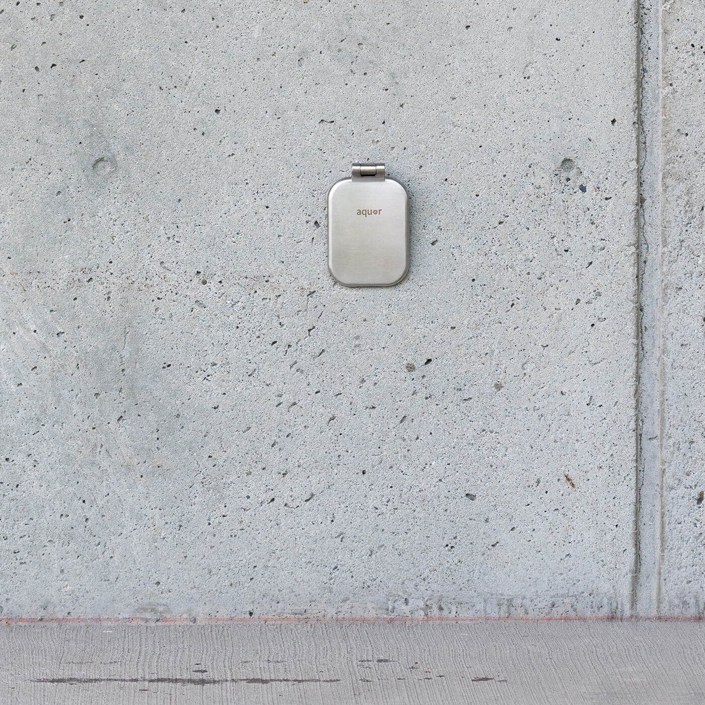 Brushed stainless steel hydrant cover mounted on concrete surface with hinge at top.