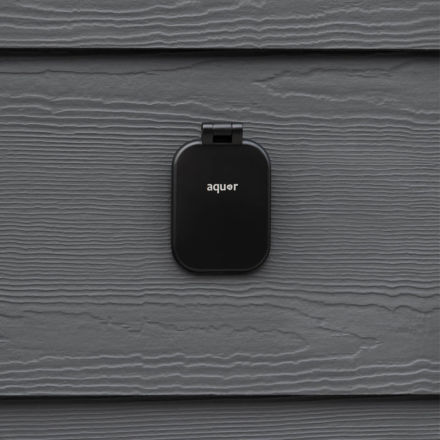 Matte black hydrant cover with rounded rectangular shape and hinge bracket mounted on textured gray surface.