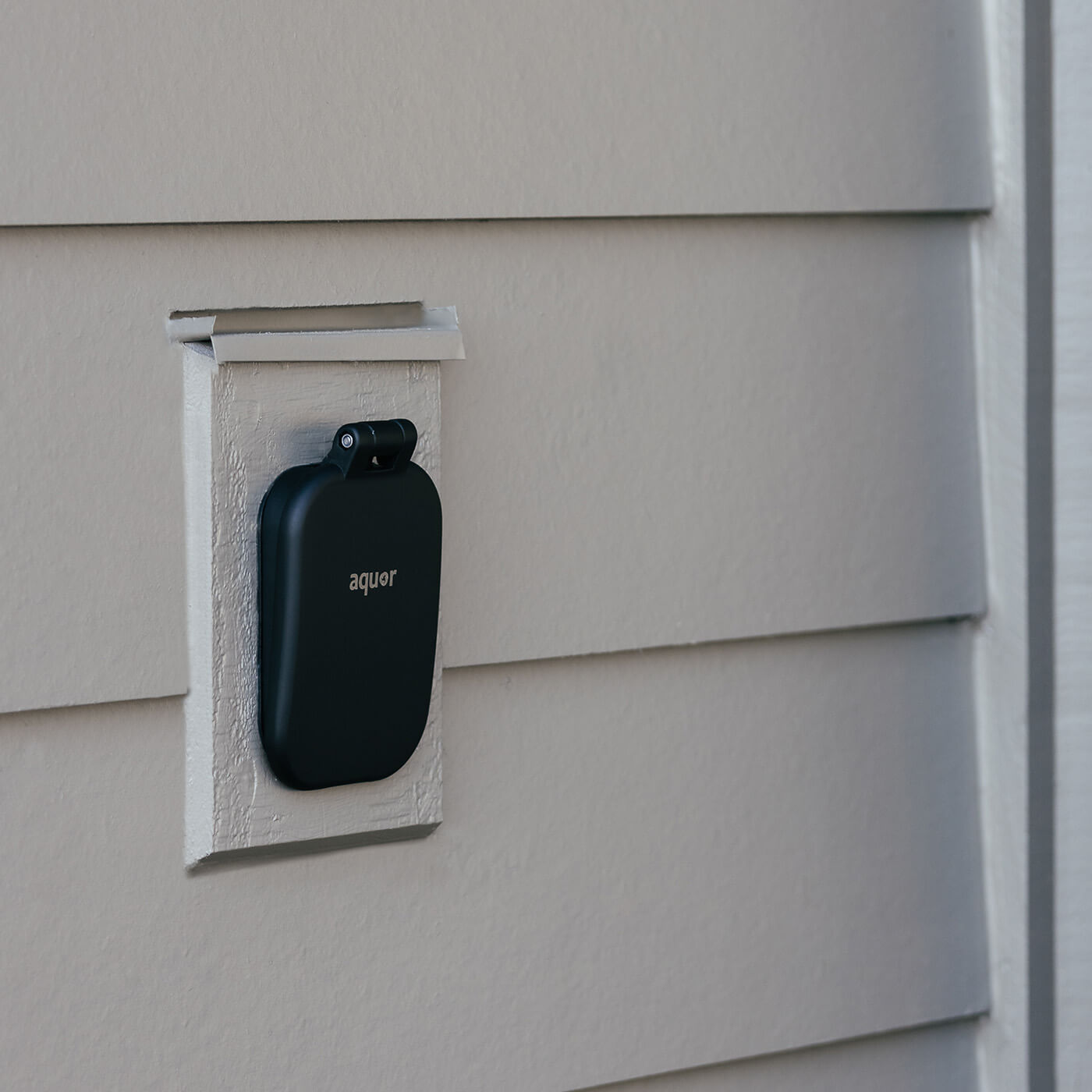 Matte black hydrant cover mounted on white exterior wall with hinged roof panel.