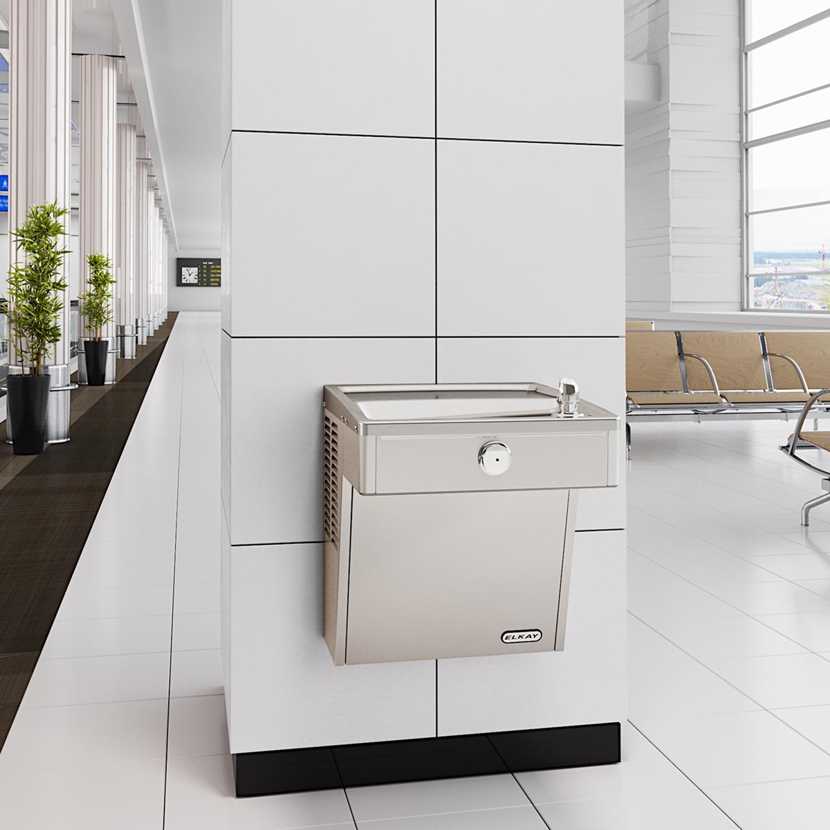 Stainless steel wall-mounted water cooler with shallow basin and single drinking spout in modern office interior.