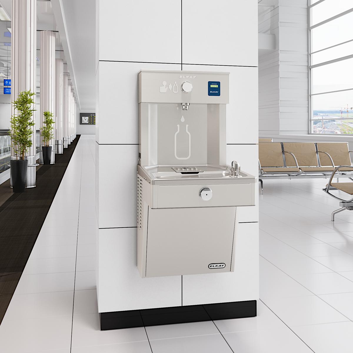 Stainless steel water filling station with refrigerated cooler and bottle fill opening, mounted on white wall in modern offic