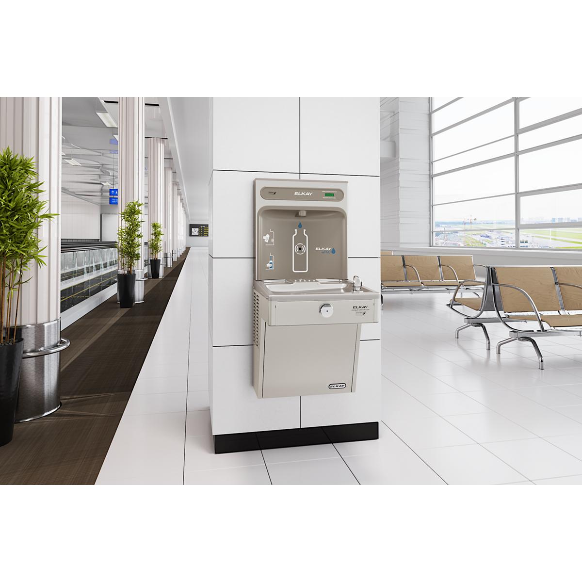 Stainless steel water cooler and bottle filling station mounted on wall in modern office space with seating area.