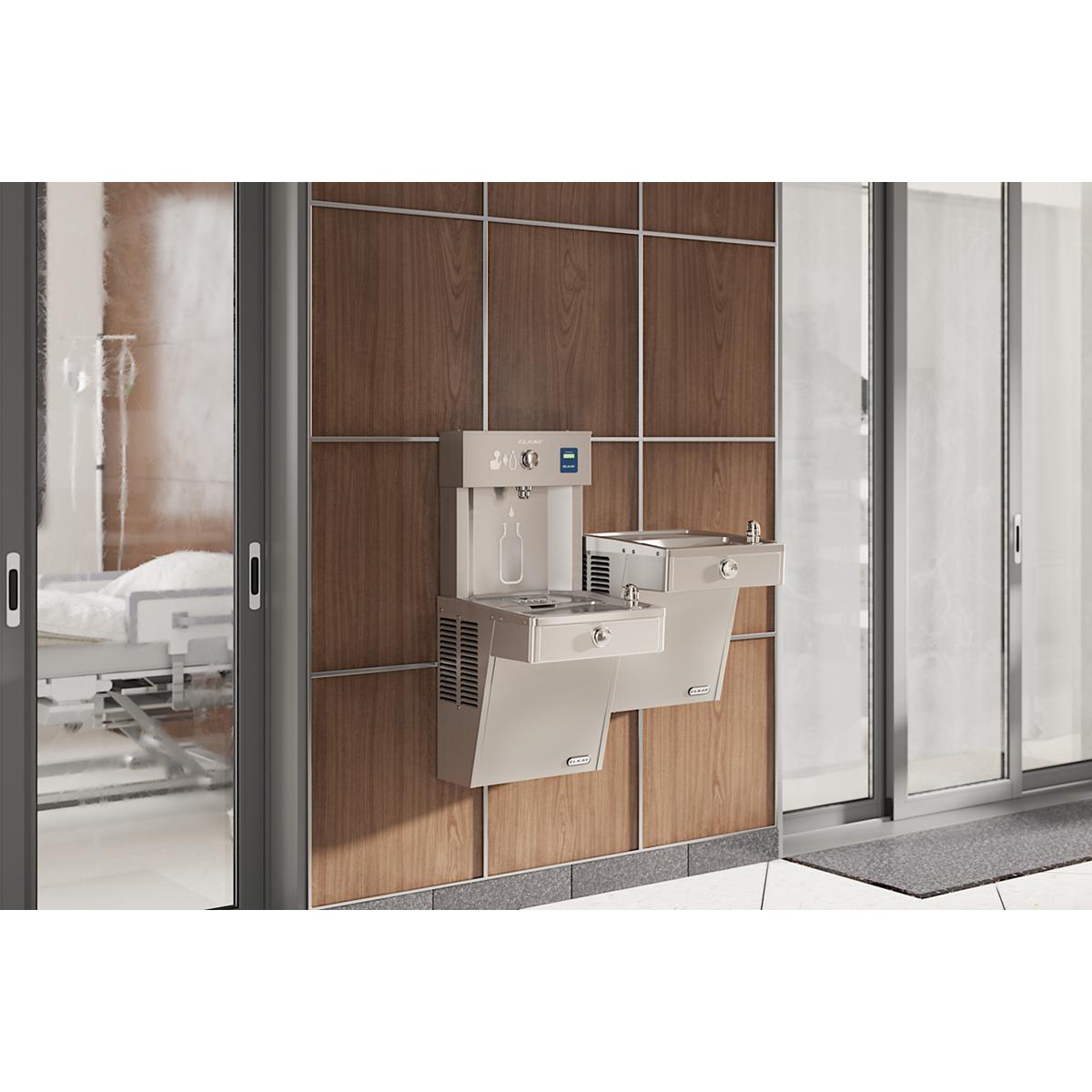 Stainless steel wall-mounted water fountain with upper bottle filling station and lower drinking basin in institutional hallw