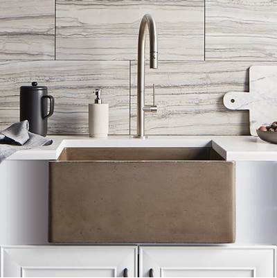 Earth-toned farmhouse sink with curved front apron, stainless steel arc faucet, and light wood tile backsplash.
