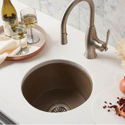 Earth-tone round undermount bar sink with matching bronze faucet on white marble countertop.