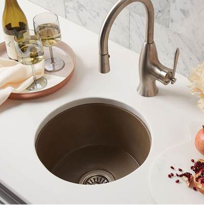 Earth-tone round undermount bar sink with matching bronze faucet on white marble countertop.