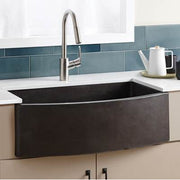 Slate farmhouse sink with curved front, stainless steel pull-down faucet, installed in white countertop with blue tile backsp