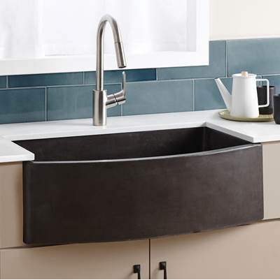 Slate farmhouse sink with curved front, stainless steel pull-down faucet, installed in white countertop with blue tile backsp