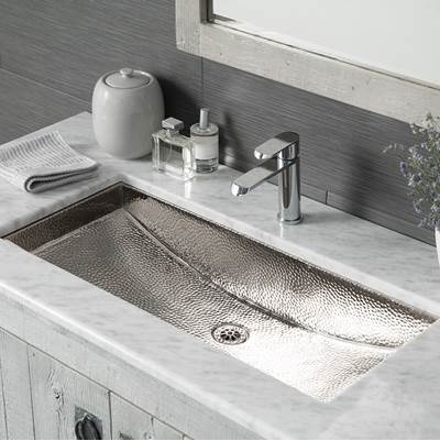 Polished nickel trough sink with hammered surface texture mounted in white marble countertop with faucet and drain.