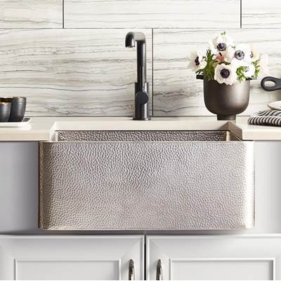 Brushed nickel farmhouse sink with hammered copper exterior and single black faucet installed in white cabinetry.
