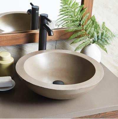 Round concrete bathroom sink with black faucet on wood and stone countertop.