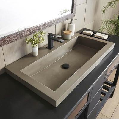 Rectangular concrete trough sink in earth tone with integrated drain, mounted on dark vanity in bathroom setting.