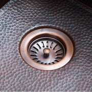 Copper basket strainer with radial slot design installed in hammered copper sink bowl.